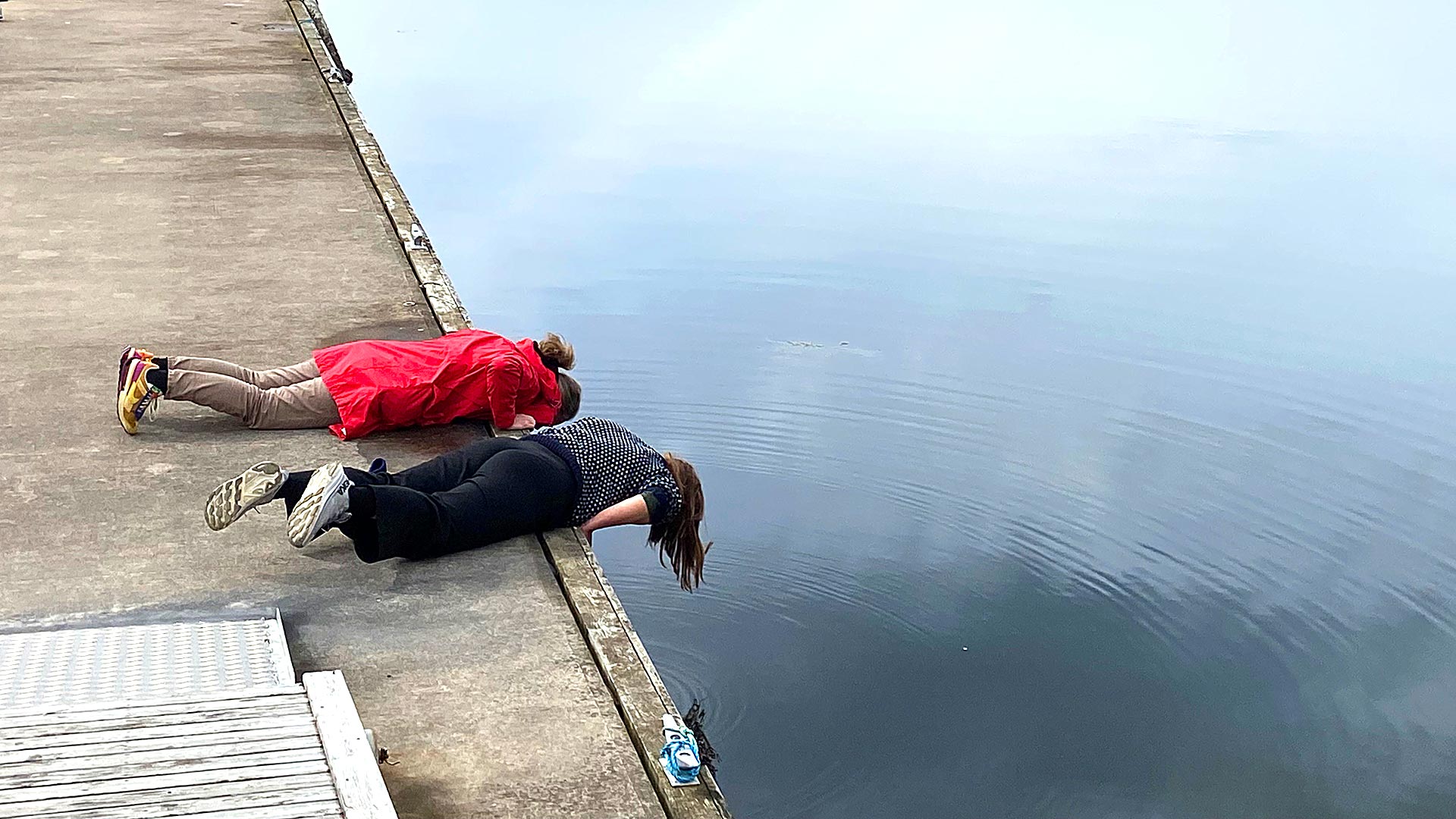 Two people lying on the jetty looking into the water